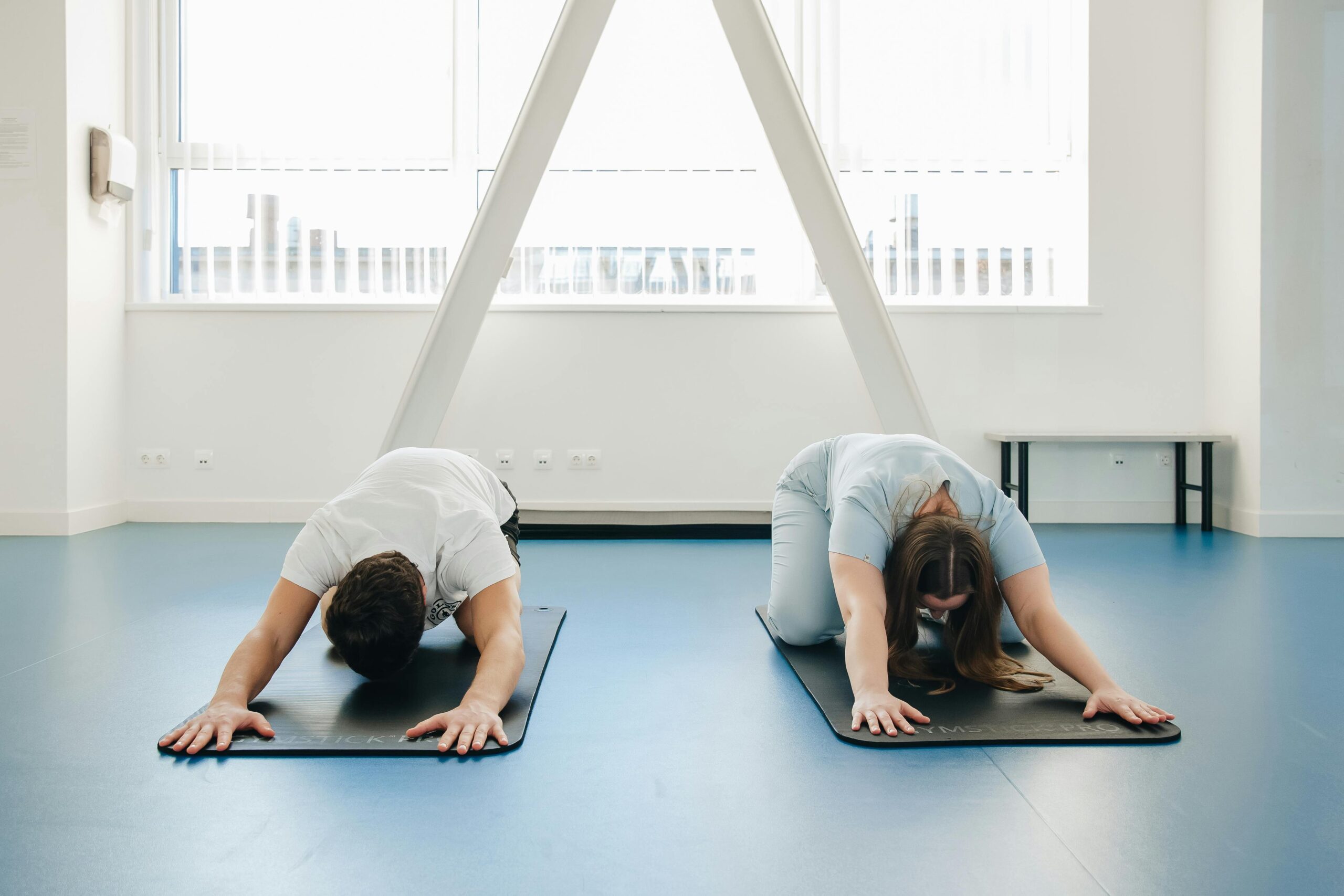 Two individuals practicing yoga in a modern clinic setting, focusing on relaxation and sciatica exercises