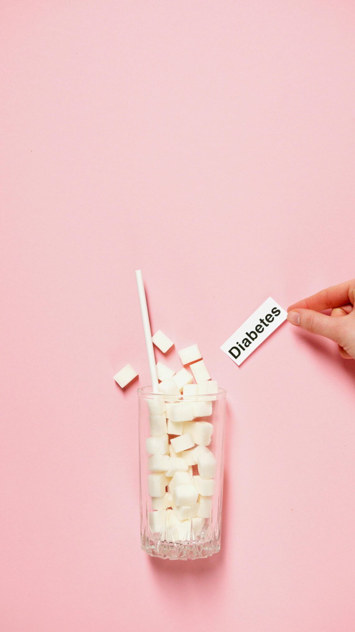 Glass of sugar cubes with diabetes label on pink background. prediabetes vs diabetes