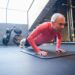 Senior man doing push-ups on a mat in a gym setting, emphasizing fitness. Learn the benefits of exercise for older adults.