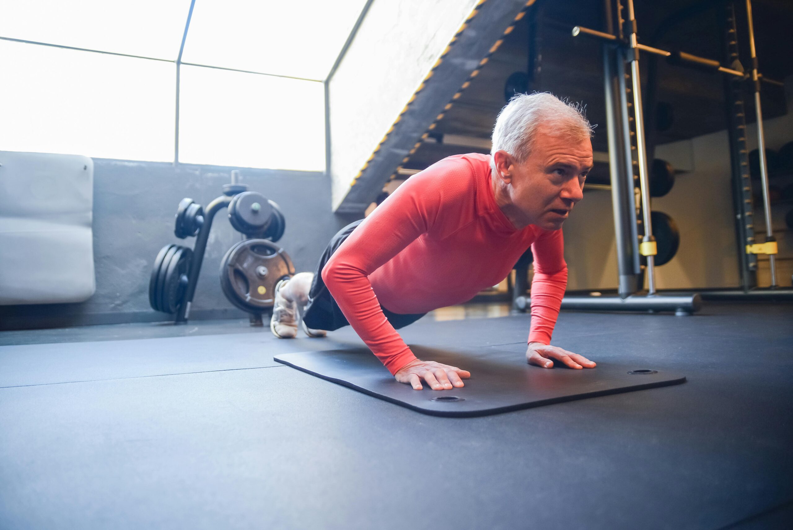 Senior man doing push-ups on a mat in a gym setting, emphasizing fitness. Learn the benefits of exercise for older adults.
